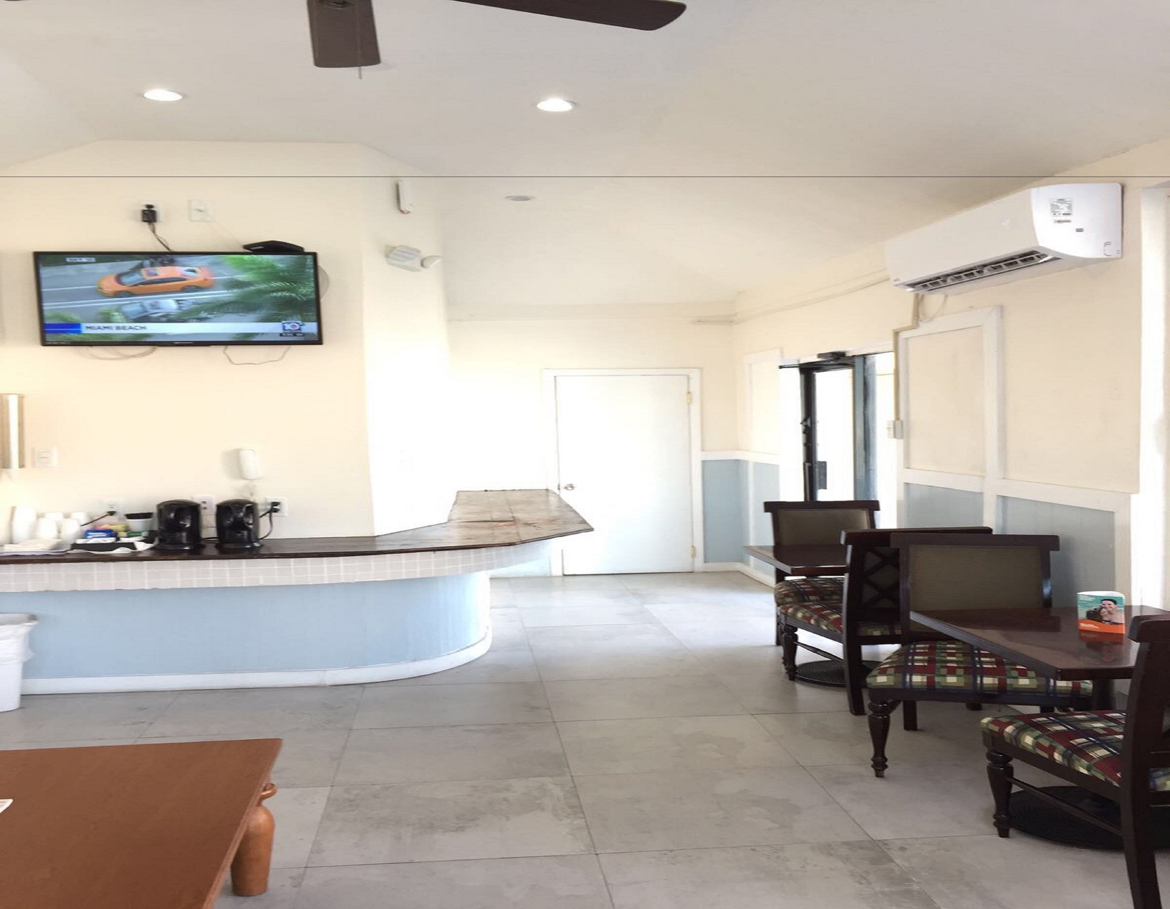 Een hotel lobby met een gebogen receptiebalie, een aan de muur bevestigde televisie en een zithoek met stoelen en een tafel.