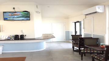 A hotel lobby with a curved reception desk, a television mounted on the wall, and a seating area with chairs and a table.