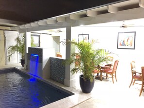 A pool area with a blue-lit water feature, potted plants, and outdoor seating. - The Colony Club Inn & Suites (Nassau)