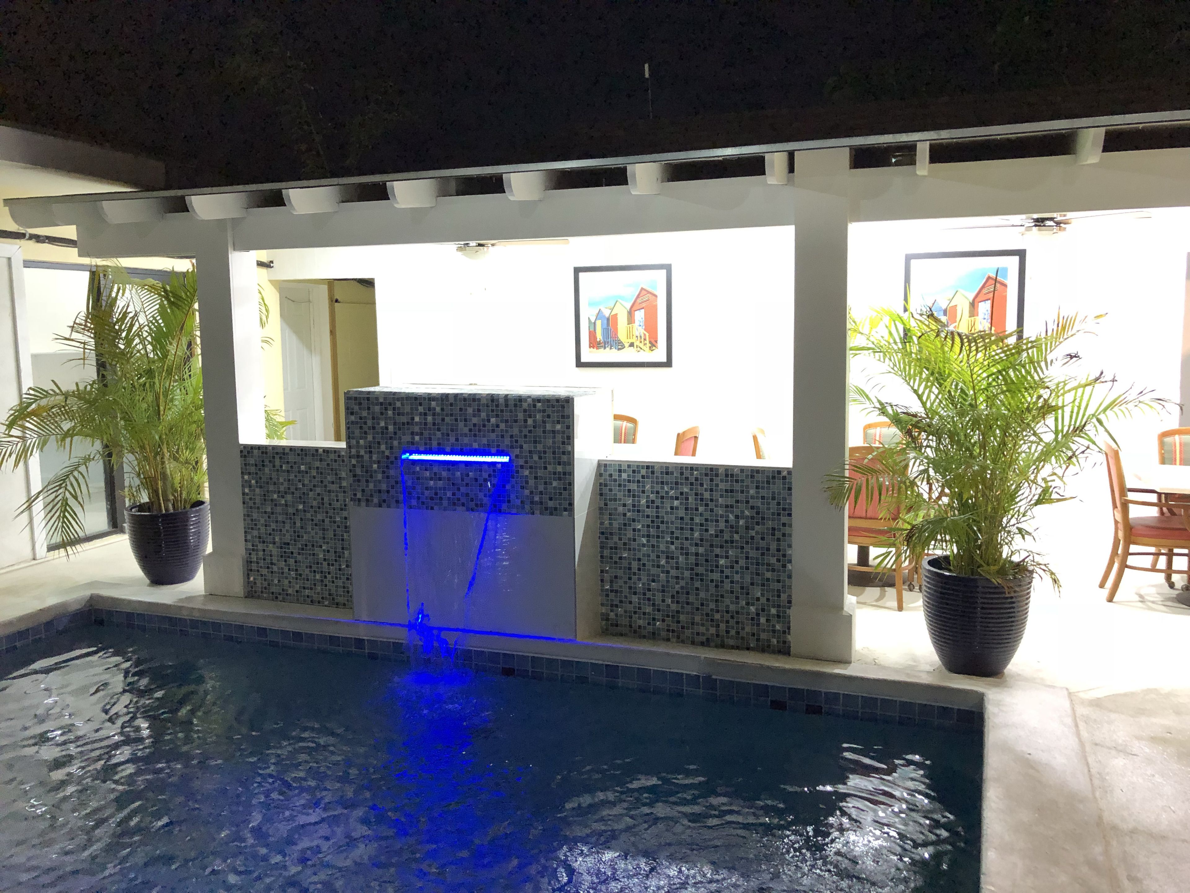 A pool area with a blue-lit water feature, tiled walls, and potted plants.