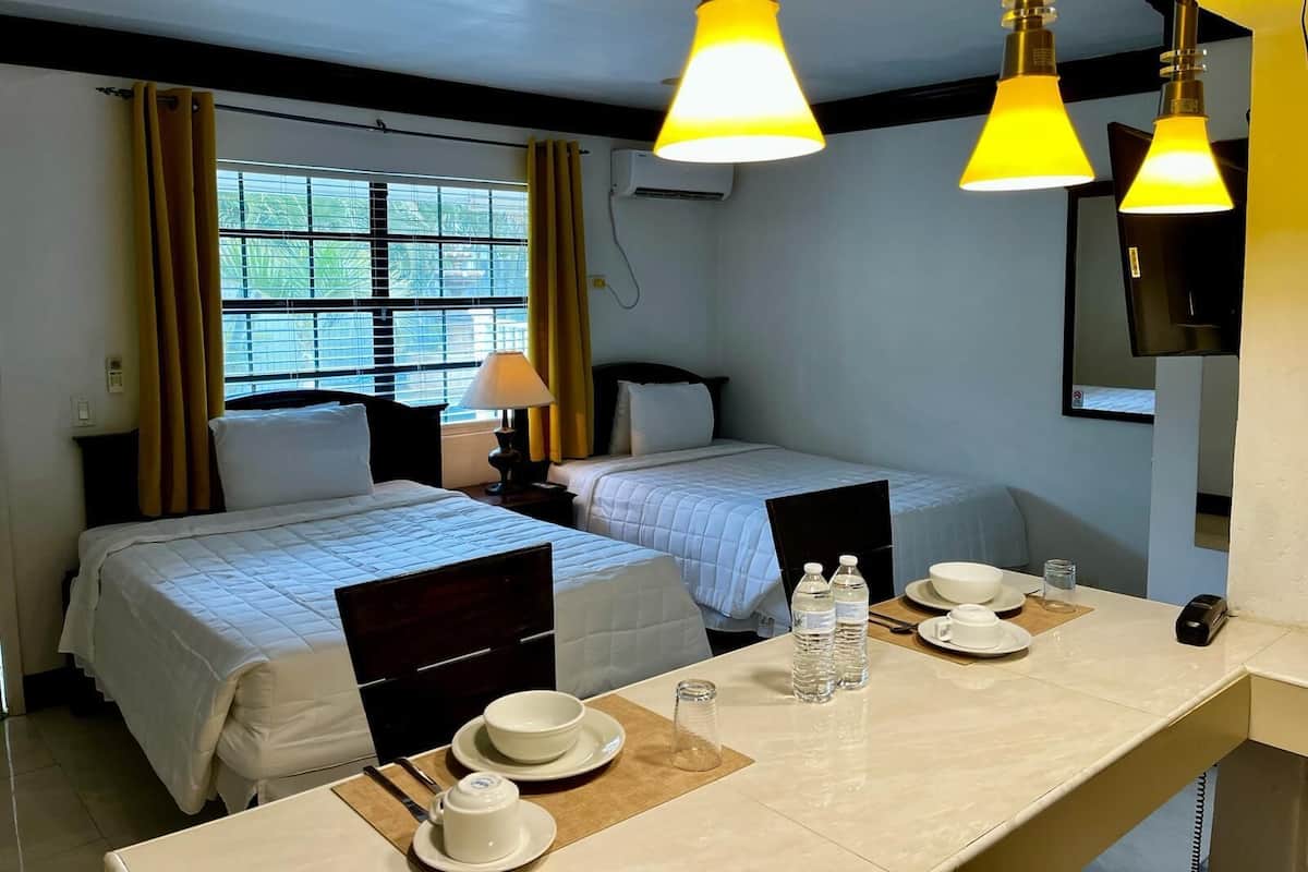 A hotel room with two beds, a desk with a lamp, a TV, and a window with curtains.
