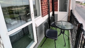 A balcony with a glass door, a small table with chairs, and artificial grass flooring.
