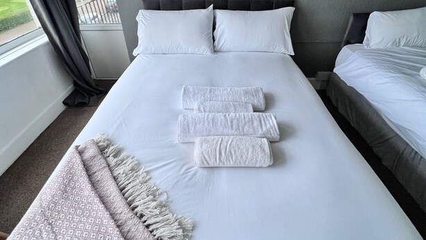 A hotel room with a large bed, two pillows, a bedside table, and a view of the outside.