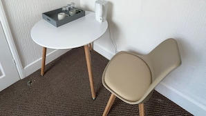 A small room with a white table, a chair, a shelf with books, and a power outlet.
