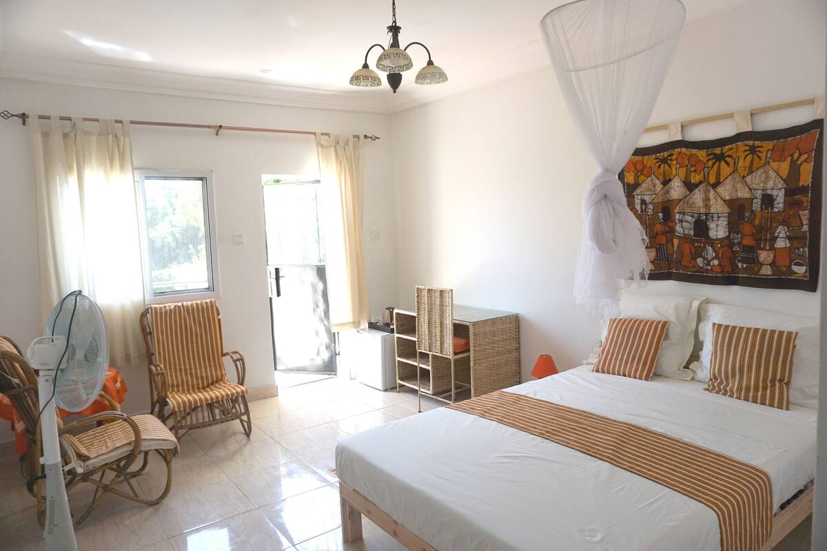 A bedroom with a bed, a chair, a desk, and a fan.