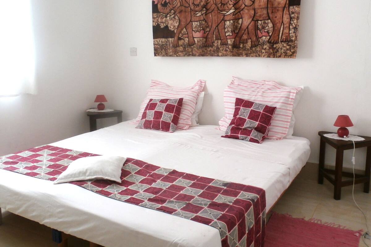 A neatly made bed with a patterned bedspread, two pillows, and a red throw blanket.