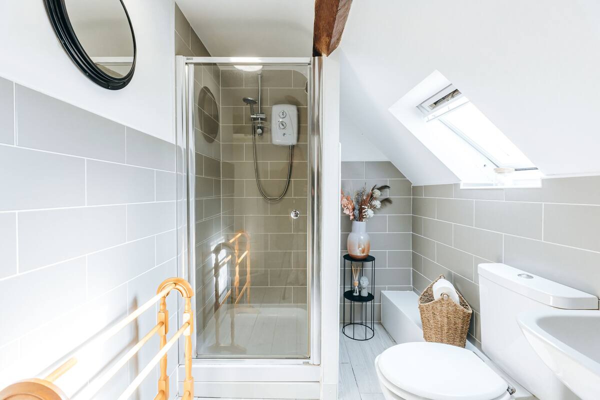 A modern bathroom with a glass-enclosed shower, a toilet, a bathtub, and a skylight.