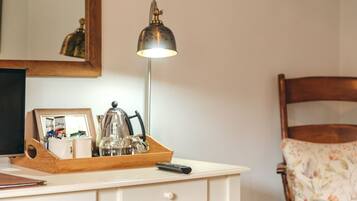 A white desk with a wooden tray holding a remote control, a picture frame, and a kettle. A mirror reflects part of the room.