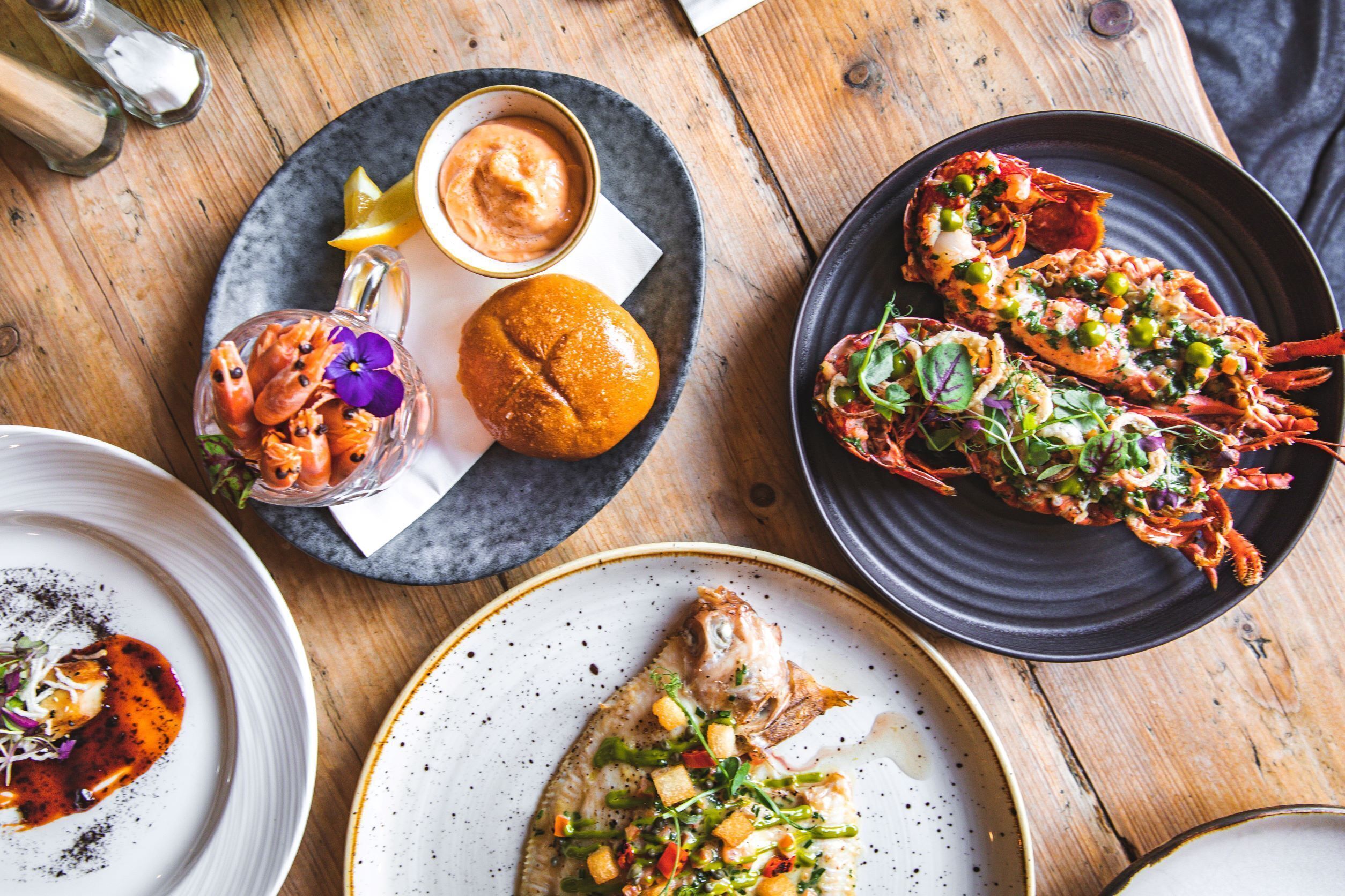 A wooden table with various dishes including seafood, a fish, and a bread roll.
