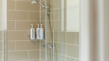 A shower area with beige tiles, a glass enclosure, and two bottles of body wash and conditioner on a shelf.