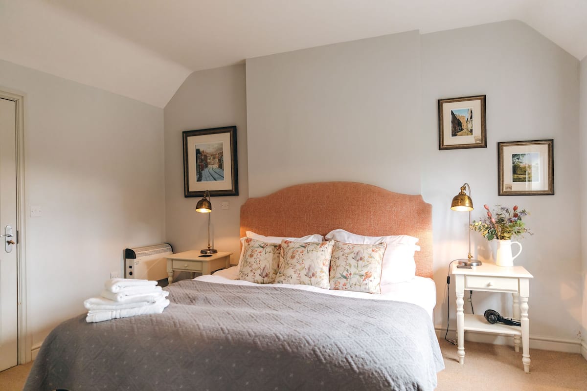 A neatly made bed with a grey blanket, a bedside table with a lamp, and a wall-mounted picture frame.