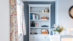 A room with a white bookshelf containing books, a radiator, and a vase with flowers. - The Pheasant at Neenton (Bridgnorth)