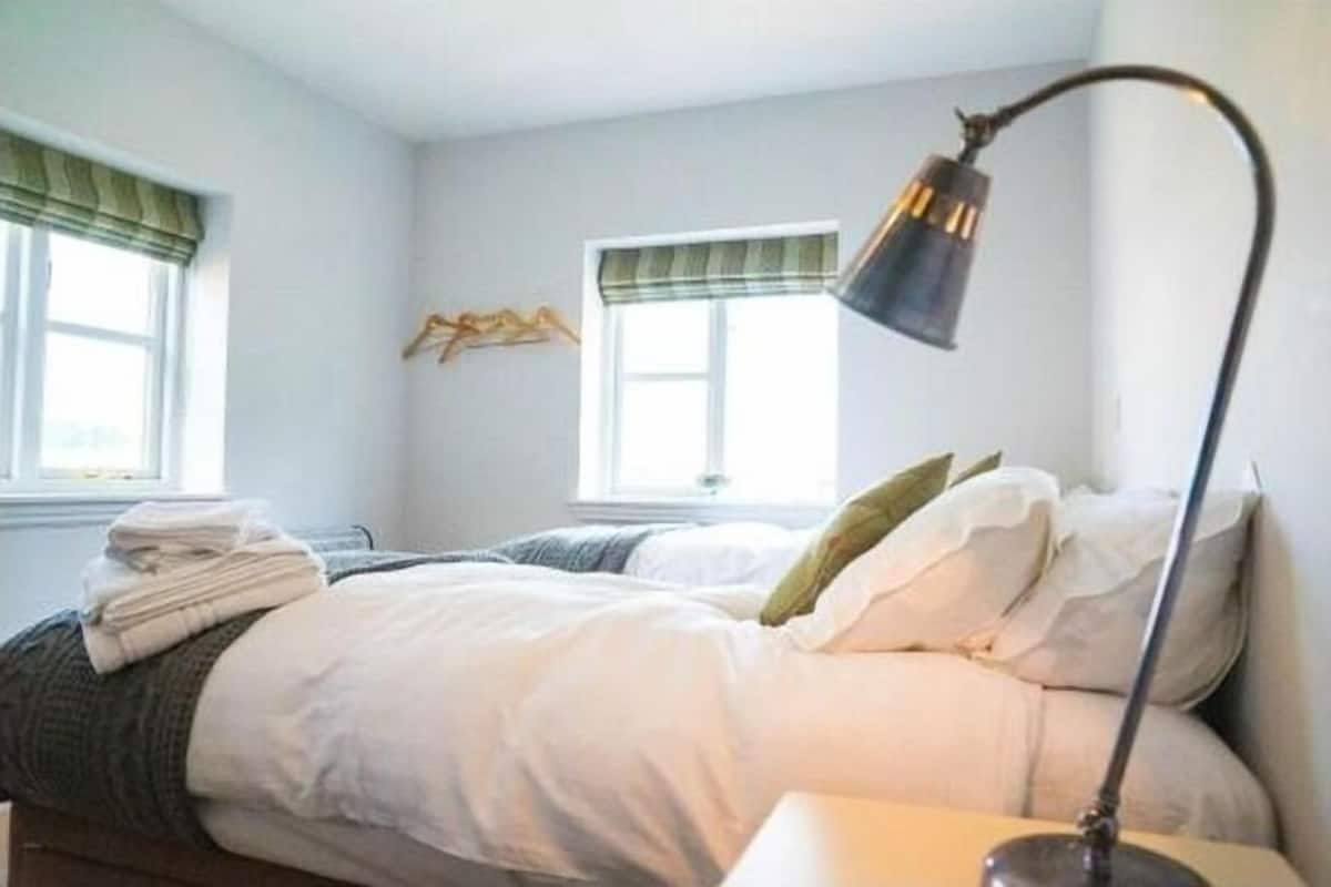 A bedroom with two beds, a bedside table, a lamp, and a window with a curtain.