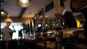 A bar with multiple taps and a person in the background. - The Pheasant at Neenton (Bridgnorth)