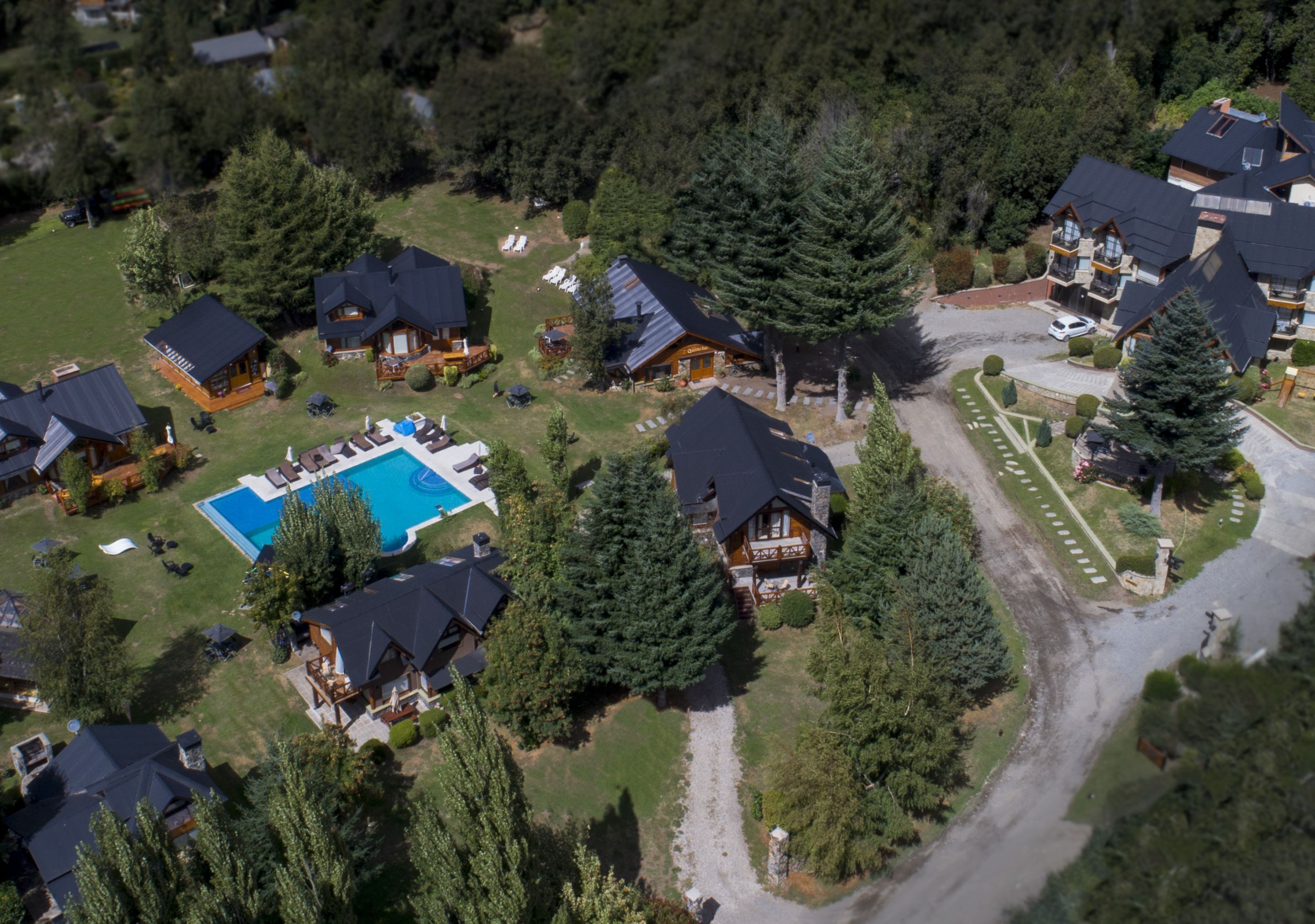 An aerial view of a residential area with multiple houses, a swimming pool, and a well-maintained lawn.