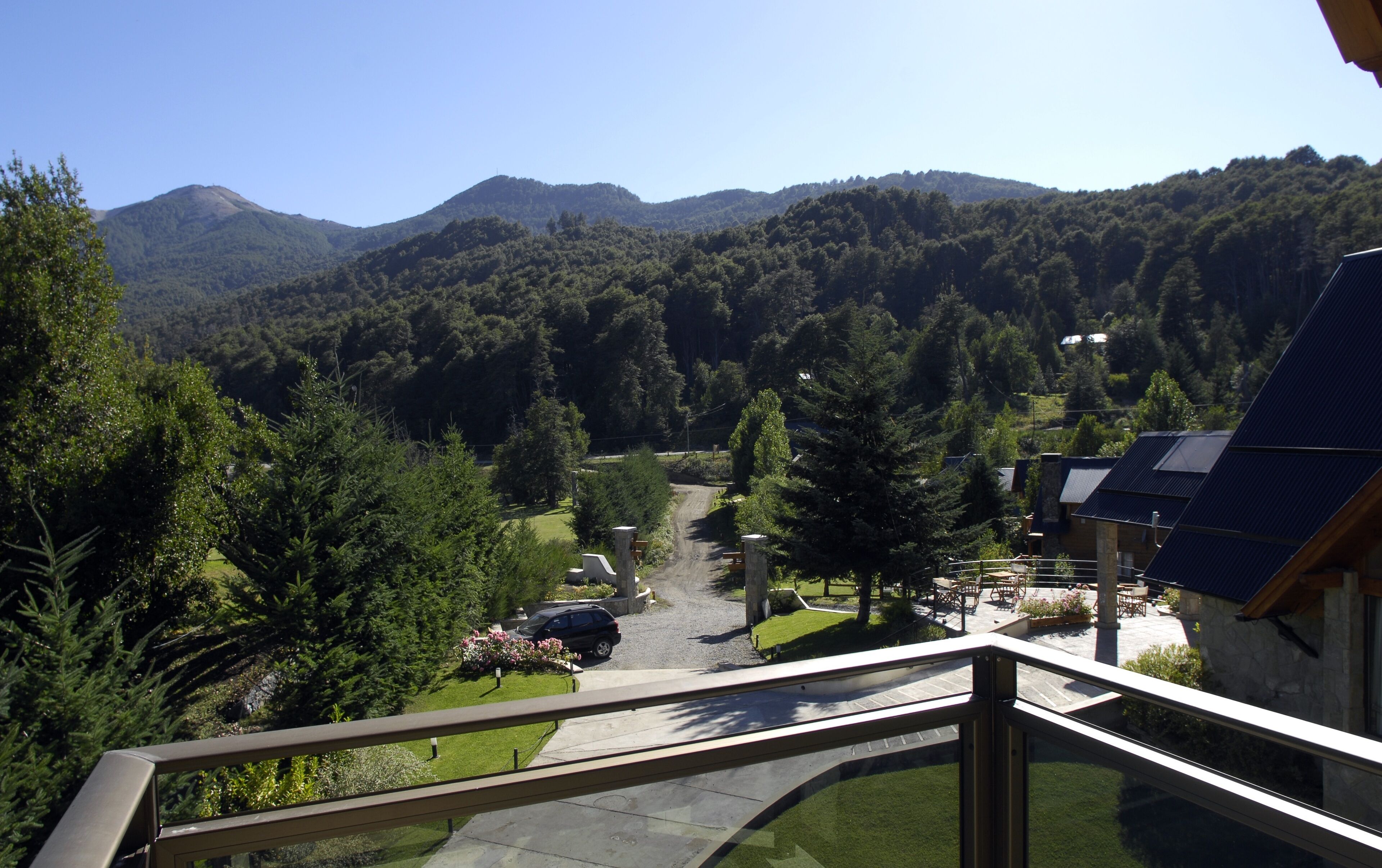 A scenic view from a balcony overlooking a mountain path, with a building featuring solar panels and a stone facade.
