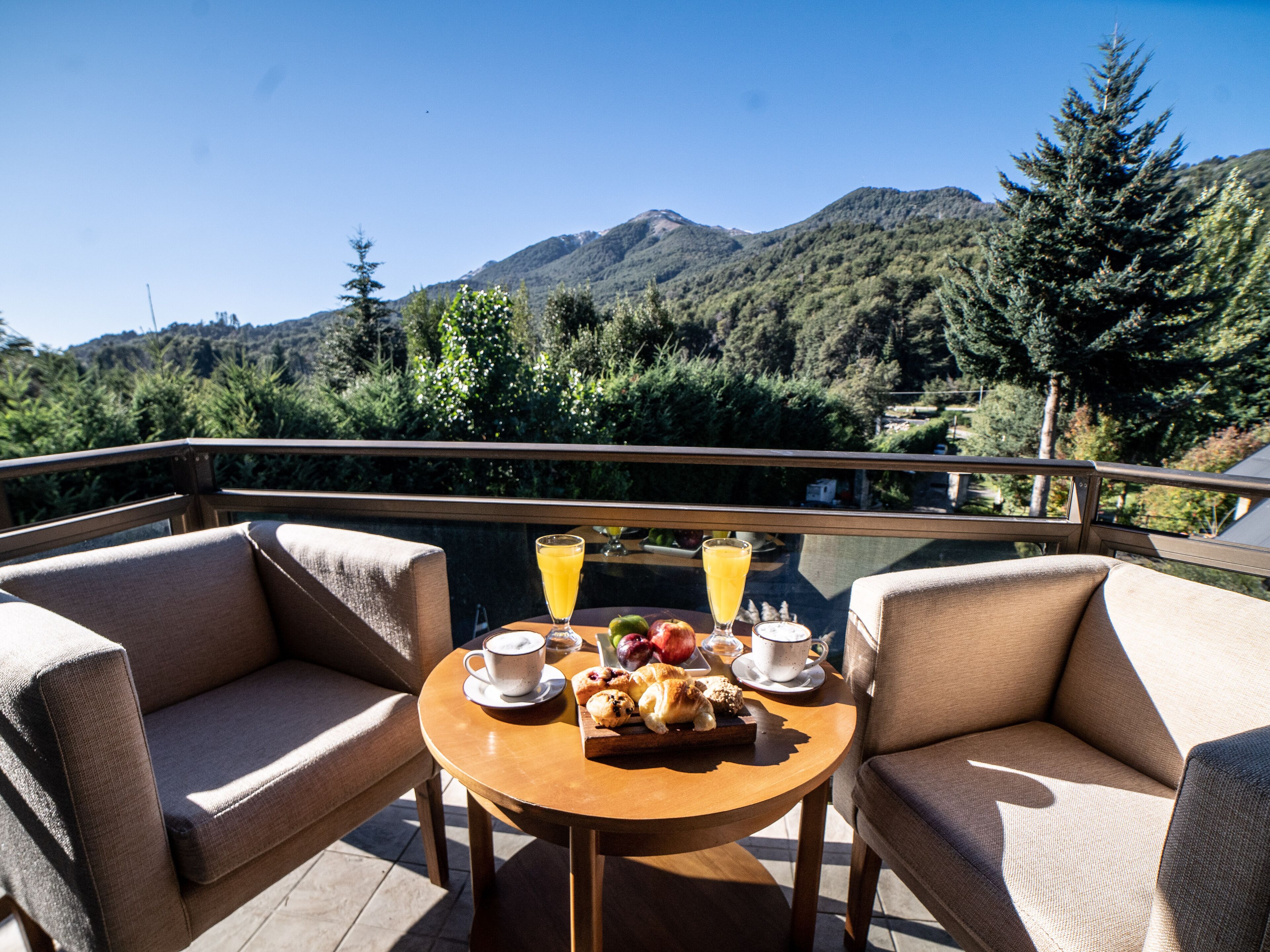 Una mesa con alimentos para el desayuno y bebidas en un balcón con vistas a un paisaje montañoso.