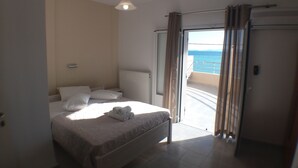 A bedroom with a bed, a radiator, a window with curtains, and a view of the sea. - Harbour View - Oceanis Apartments (Kefalonia)