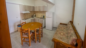A compact kitchen with a dining table and chairs, a refrigerator, and a stove. - Harbour View - Oceanis Apartments (Kefalonia)