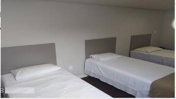 Habitación con tres camas individuales colocadas una junto a la otra, cada una con cabecero y ropa de cama blanca.