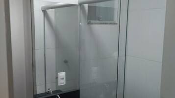 A modern bathroom with a glass shower enclosure, a black sink with a mirror, and a small window above the shower.