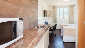 A compact hotel room with a kitchenette, a bed, a desk, and a chair. - Front Hotel Expominas (Belo Horizonte)