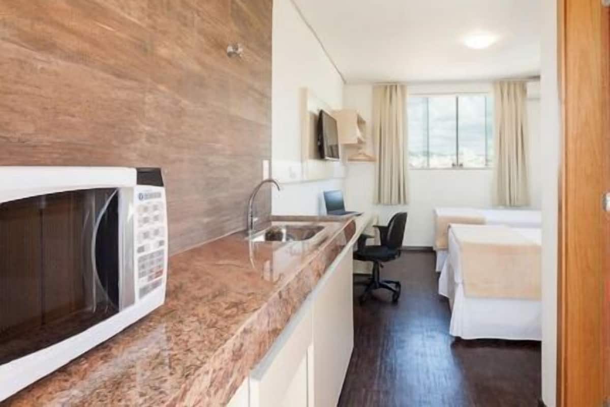 A compact hotel room with a kitchenette, a bed, a desk, and a chair.