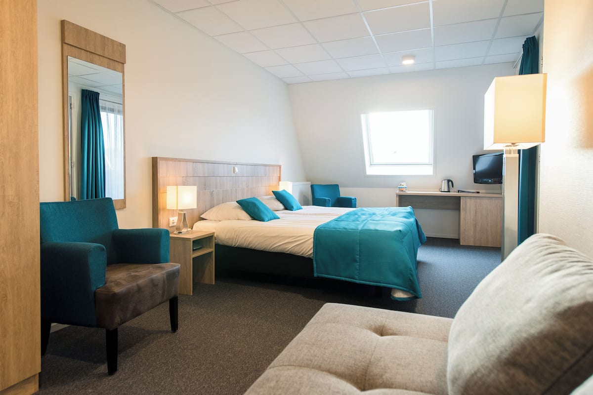 A hotel room with a bed, a desk, a chair, a TV, and a window.