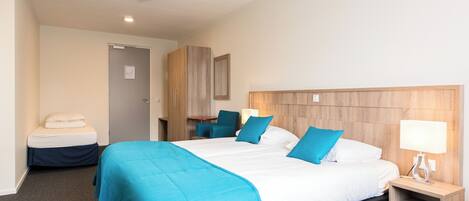 Quarto de hotel com uma cama grande, mesa de cabeceira com abajur, escrivaninha com cadeira e guarda-roupa.
