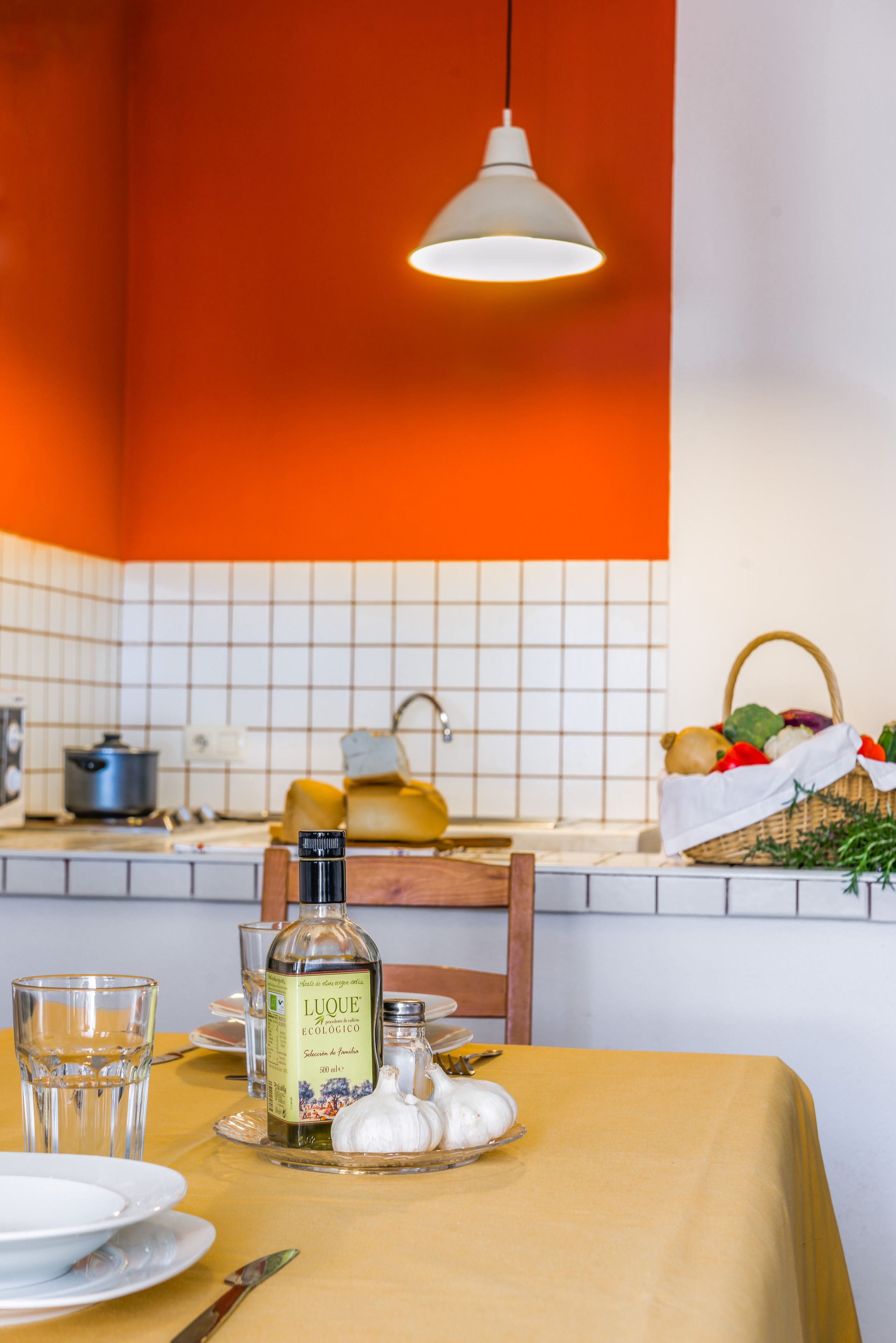 A kitchen with a yellow table, a bottle of liquor, glasses, and a basket of vegetables.