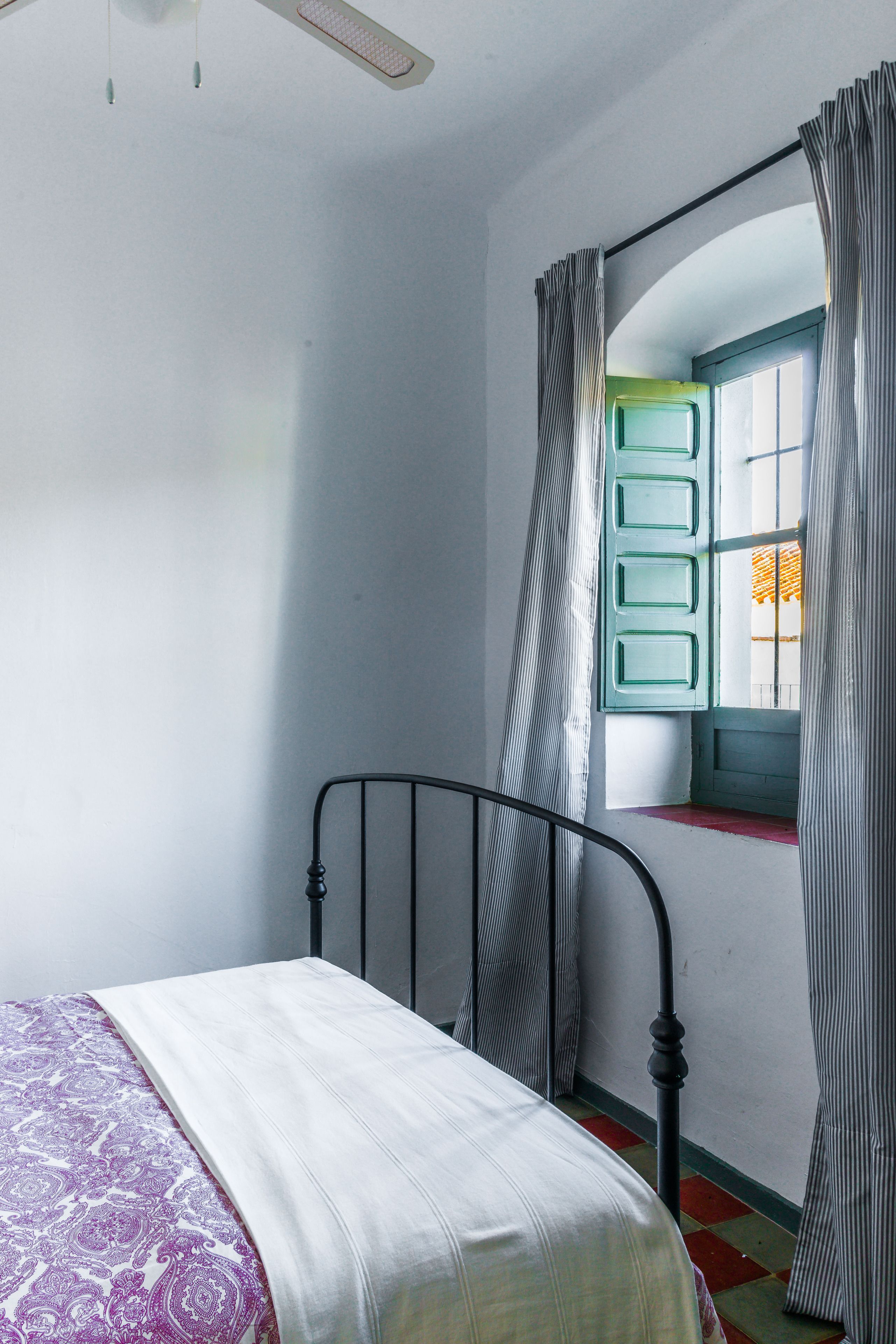 Een slaapkamer met een enkel bed, een raam met gordijnen en een deur met een groene omlijsting.