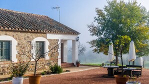 Un edificio de piedra con techo de tejas, mesas al aire libre y plantas en macetas.