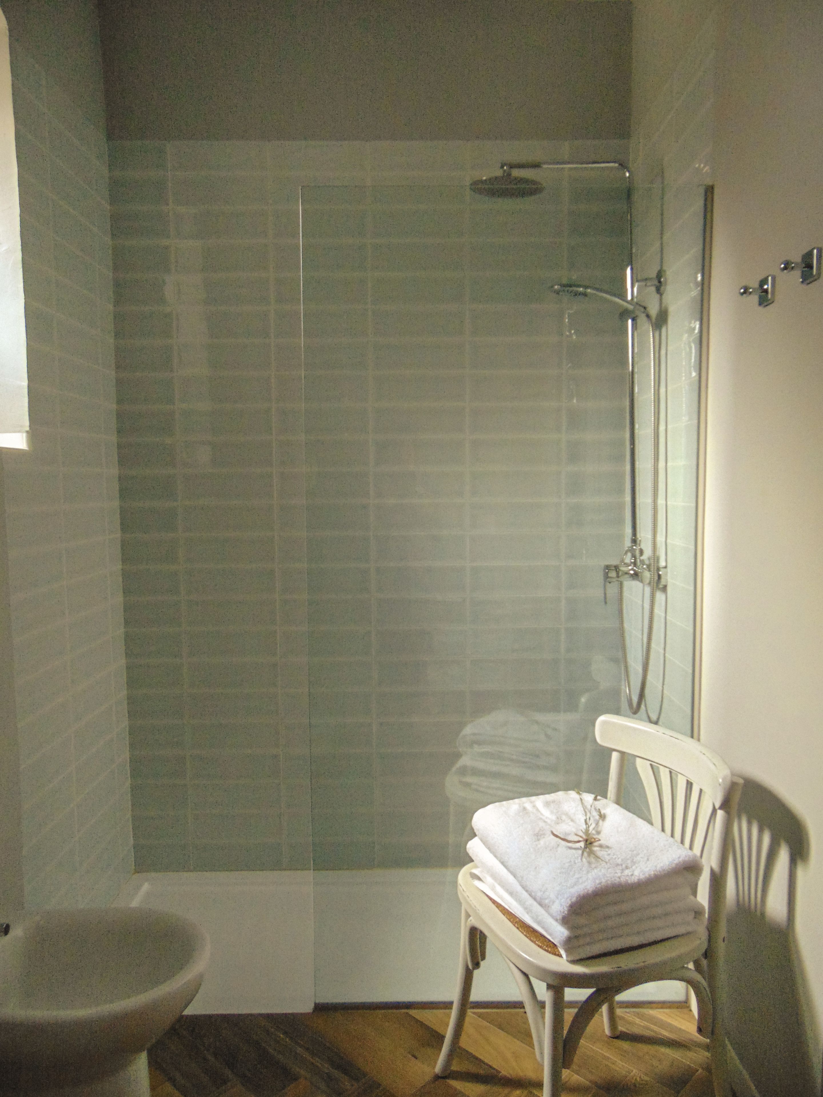 Ein Badezimmer mit Duschkabine aus Glas, einem weißen Waschbecken und einem Sessel mit Handtüchern.