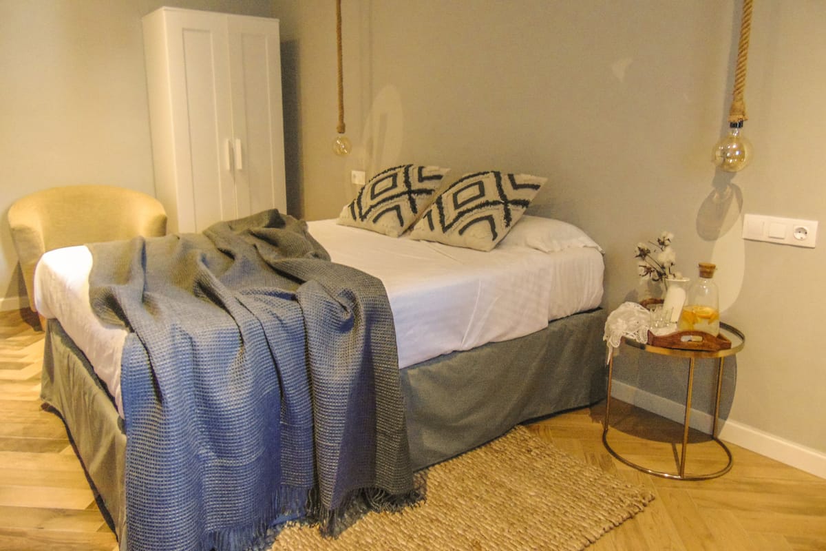 Un dormitorio con cama, una silla, una mesita de noche con lámpara y un armario.