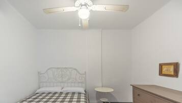 Een slaapkamer met een bed, een plafondventilator, een klein rond tafeltje en een dressoir.