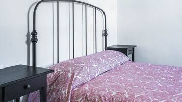 Una cama individual con estructura metálica, una mesita de noche y un velador.