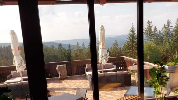 A cozy outdoor seating area with wooden furniture and a view of the forest. - Horsky Hotel Hájenka (Makov)