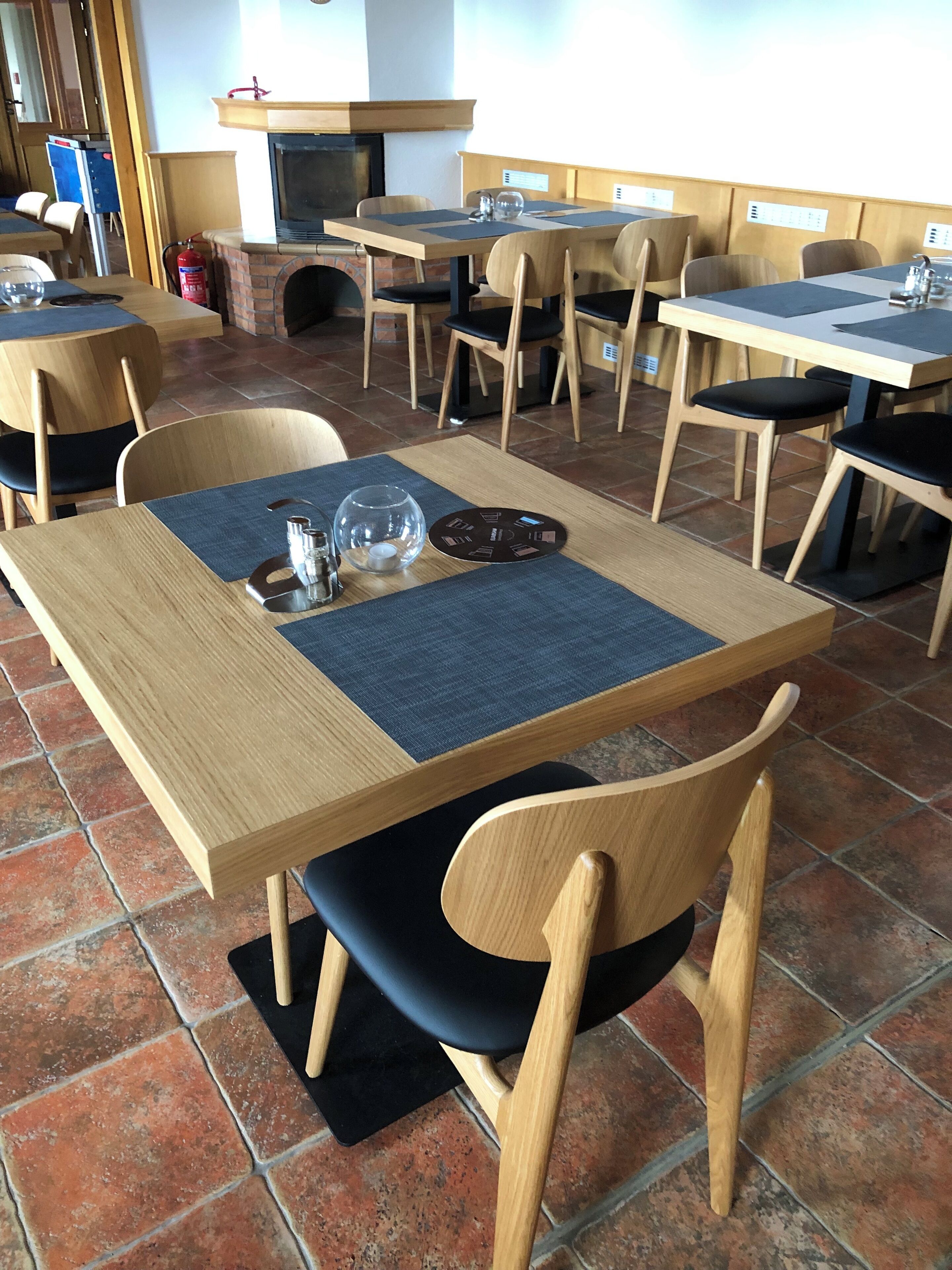 A restaurant with wooden tables and chairs, a brick fireplace, and tiled flooring.