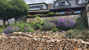 A building with multiple windows, a stone wall, and a pile of firewood. - Horsky Hotel Hájenka (Makov)