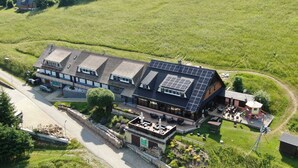 A large building with multiple levels, a covered outdoor seating area, and solar panels on the roof. - Horsky Hotel Hájenka (Makov)