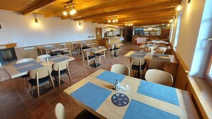 A restaurant with wooden tables and chairs, a bar area, and a view of the outdoors. - Horsky Hotel Hájenka (Makov)