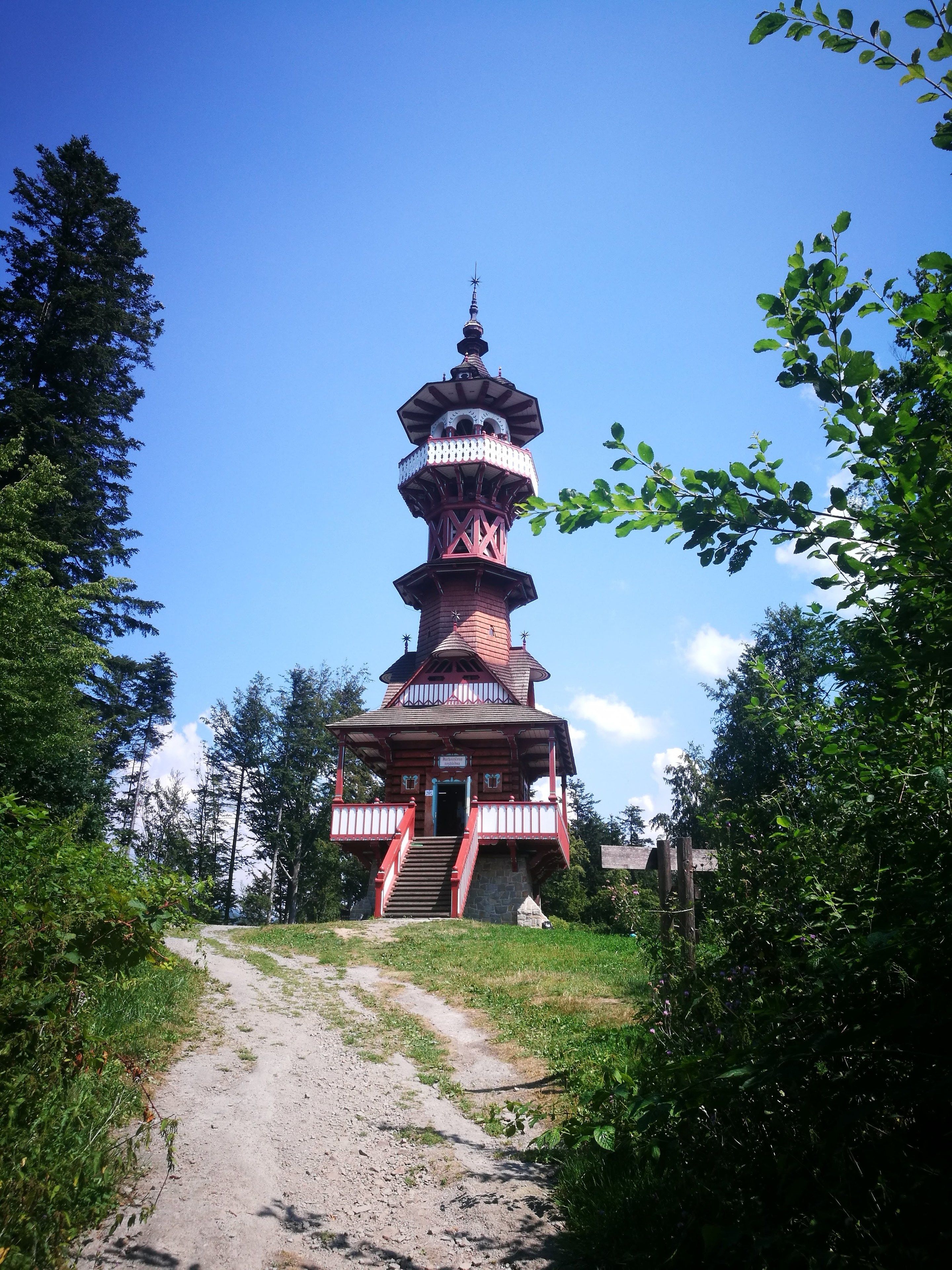 A multi-tiered pagoda-style structure with a staircase leading up to the entrance, surrounded by greenery and a clear sky.