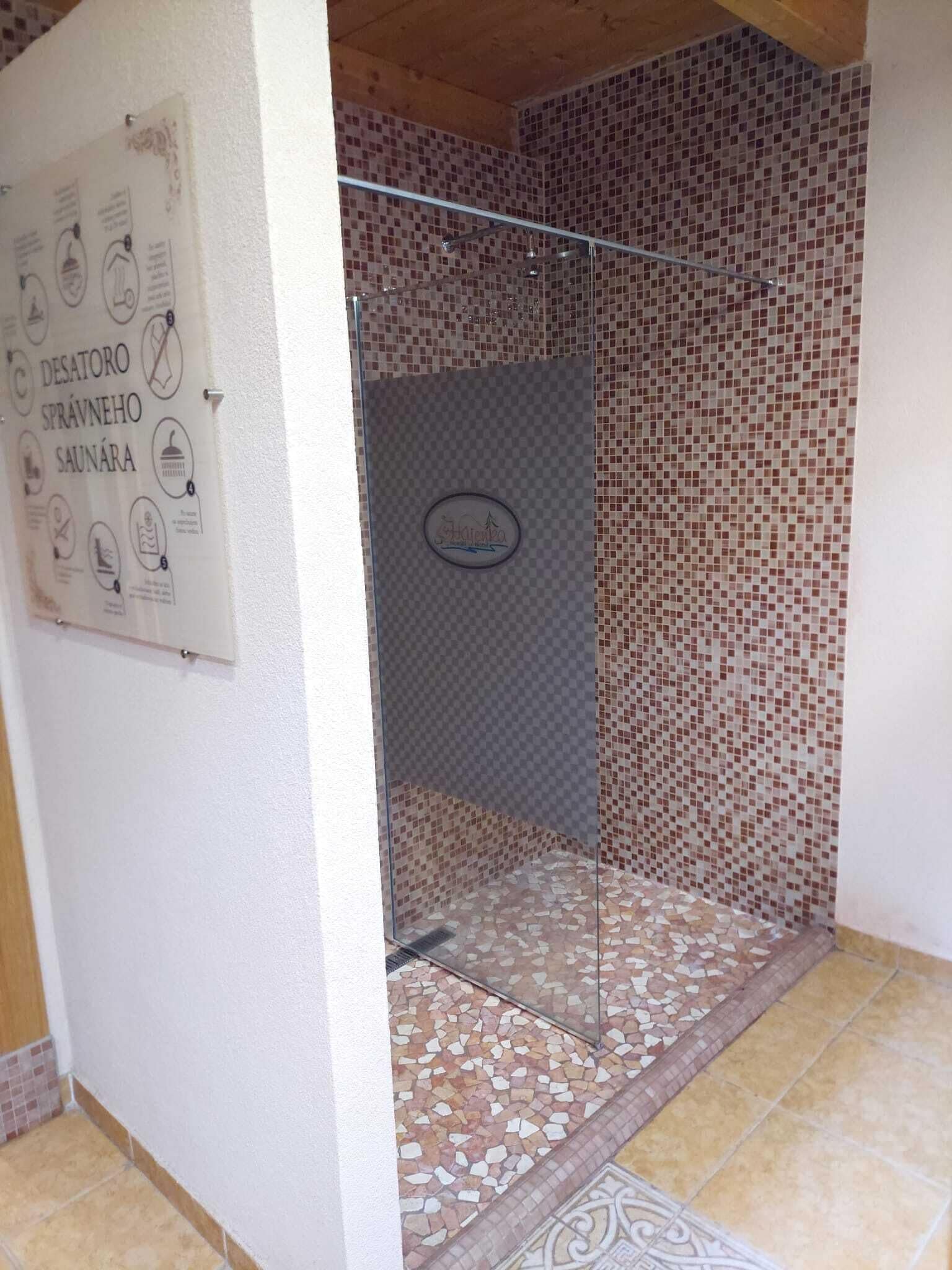 A shower area with mosaic tile walls and a glass door.