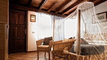 Una camera da letto rustica con parete in pietra, una porta in legno, una sedia in vimini, un letto a baldacchino e un quadro appeso al muro.