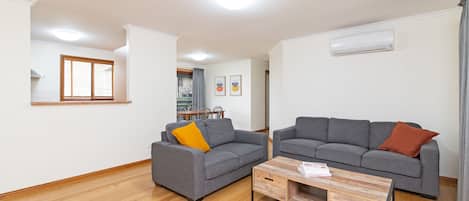 A modern living room with two grey sofas, a wooden coffee table, and a dining area in the background.