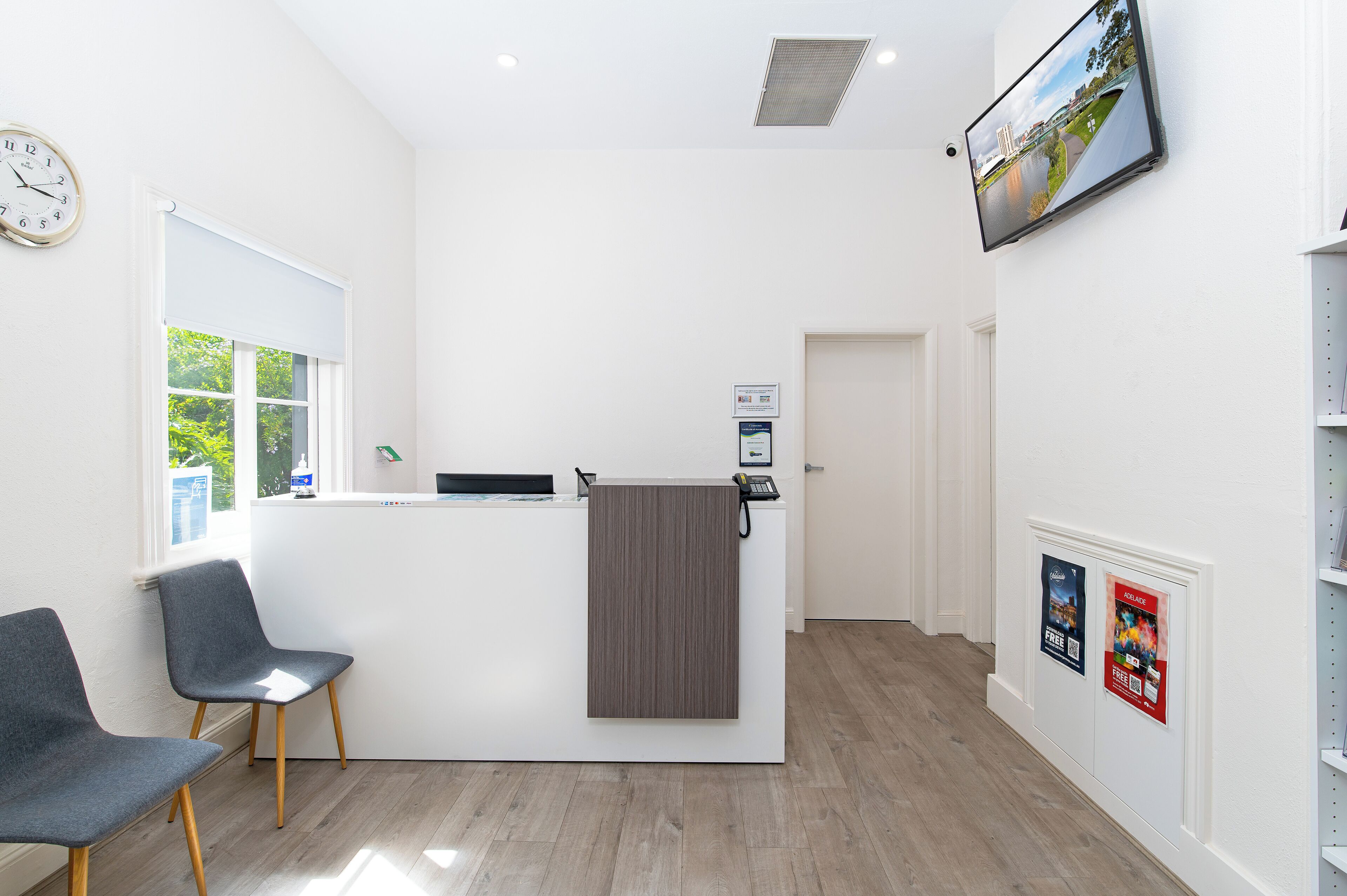 A reception area with a desk, chairs, a clock, and a TV on the wall.