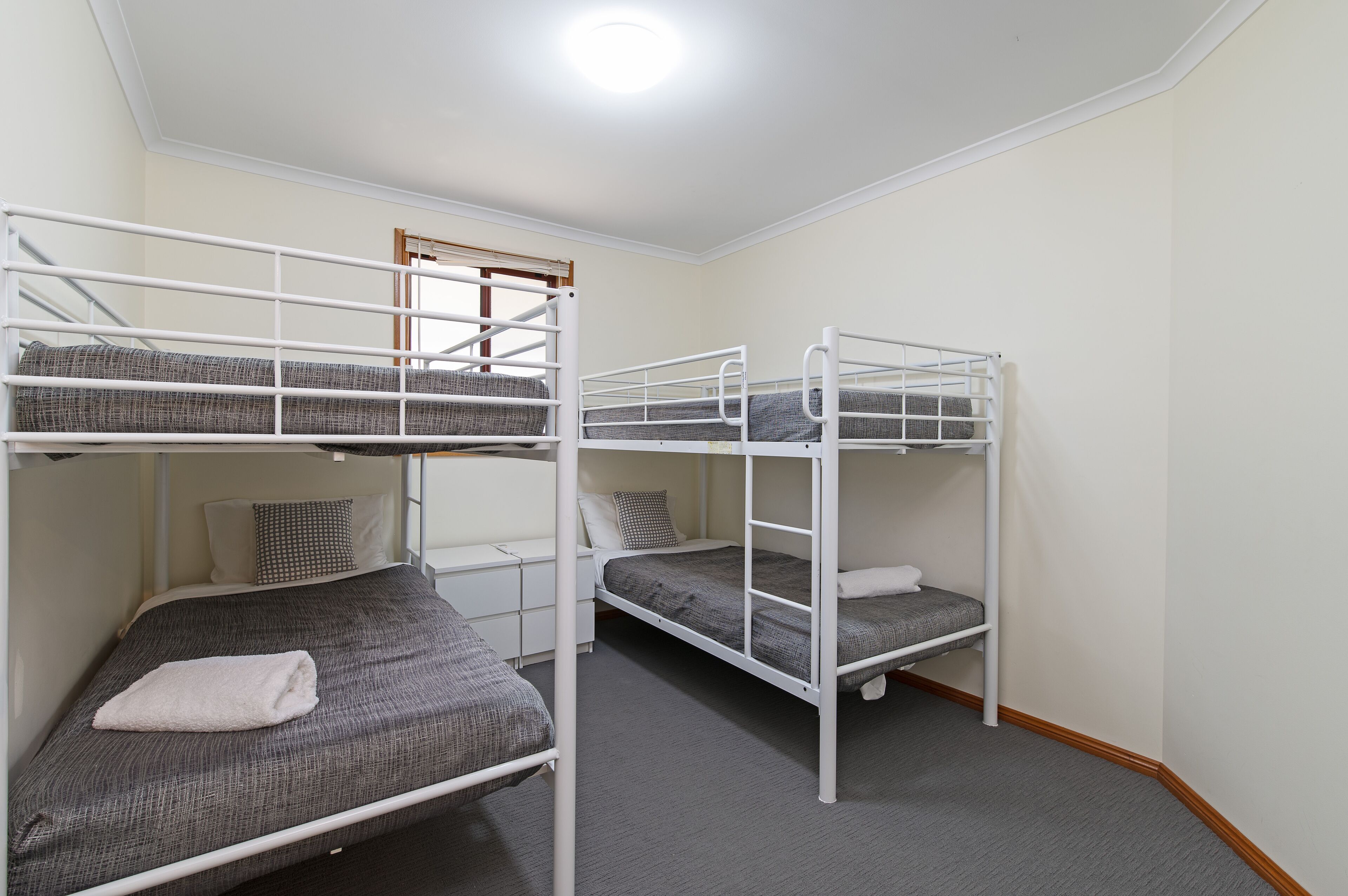 A bunk bed room with a white railing, grey bedding, and a small bedside table.