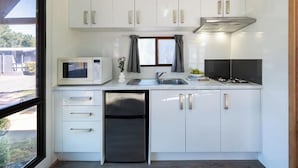 A modern kitchen with white cabinets, a built-in microwave, a stainless steel refrigerator, and a gas stove. - Adelaide Caravan Park (Hackney)