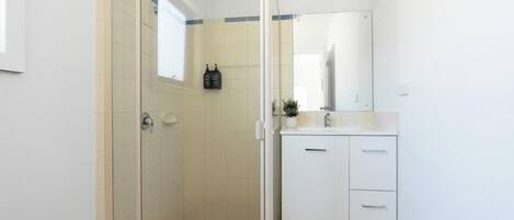 Un baño con ducha de vidrio, lavamanos blanco y espejo sobre el lavamanos.