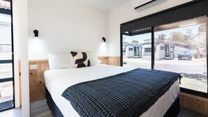 A bedroom with a bed, a window with a view of parked vehicles, and an air conditioning unit. - Adelaide Caravan Park (Hackney)